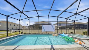 En swimmingpool med ett säkerhetsnät runt om, omgiven av en stenlagd uteplats och med utsikt över bostadshus.