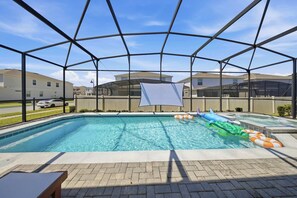 Ein Schwimmbecken mit Sicherheitsnetz, umgeben von einer gepflasterten Terrasse und Blick auf Wohnhäuser.
