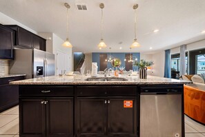 A modern kitchen with dark cabinetry, a stainless steel refrigerator, a granite countertop, and pendant lighting. - Hogwarts & Star Wars Themed Rooms, Pool, Game Room (Davenport)