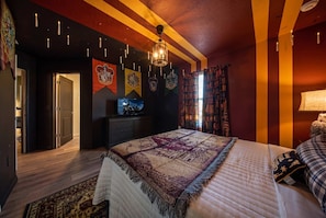 Een slaapkamer met een groot bed, een televisie, een boekenkast en een deur naar een andere kamer.