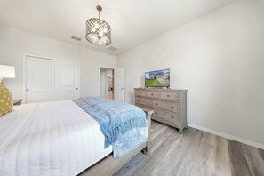 Ein Schlafzimmer mit Bett, Schminktisch und Fernseher, der ein Haus zeigt.