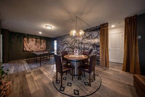 Een eetgedeelte met een ronde tafel, stoelen, een tafeltennistafel en een muur met een kaart en een steenachtige textuur.