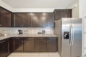 A kitchen with dark wooden cabinets, a stainless steel refrigerator, and a tiled backsplash. - Hogwarts & Star Wars Themed Rooms, Pool, Game Room (Davenport)