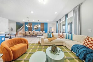 A modern living room with a sofa, orange armchair, and a dining area with a table and chairs. - Hogwarts & Star Wars Themed Rooms, Pool, Game Room (Davenport)
