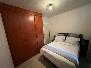 A bedroom with a bed, a wardrobe, a bedside table, and a lamp.