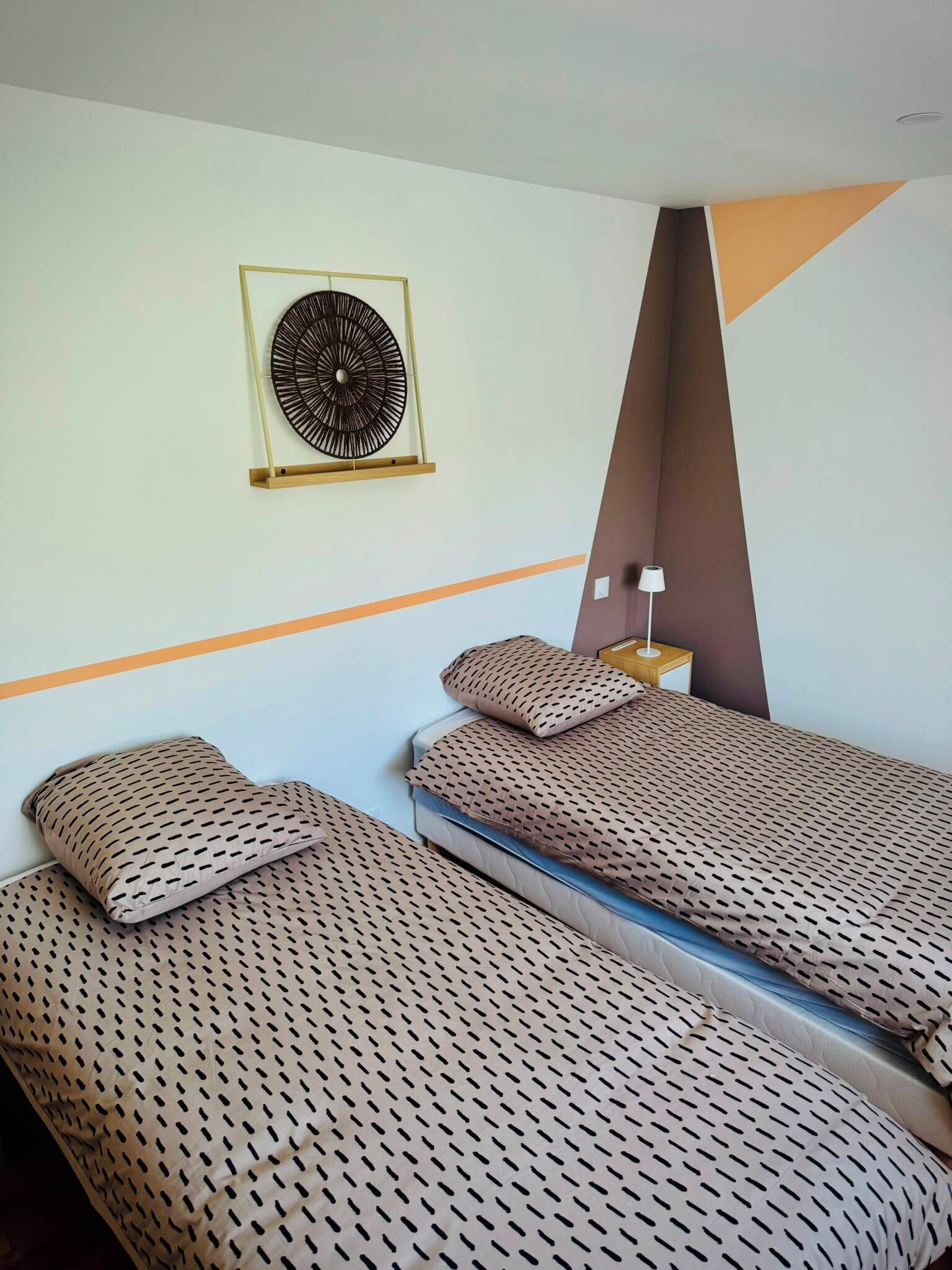 Een hotelkamer met twee eenpersoonsbedden, een ventilator aan de muur en een nachtkastje met een lamp.