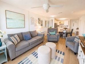 Ein Wohnzimmer mit einer Couch, Sesseln, Poufs und einem Essbereich mit Tisch und Stühlen.