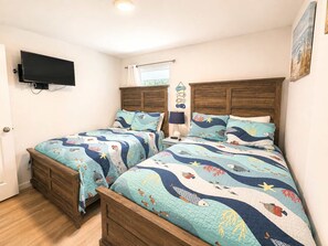 Ein Schlafzimmer mit zwei Holzbetten, einem an der Wand montierten Flachbildfernseher und einem Fenster mit Vorhängen.