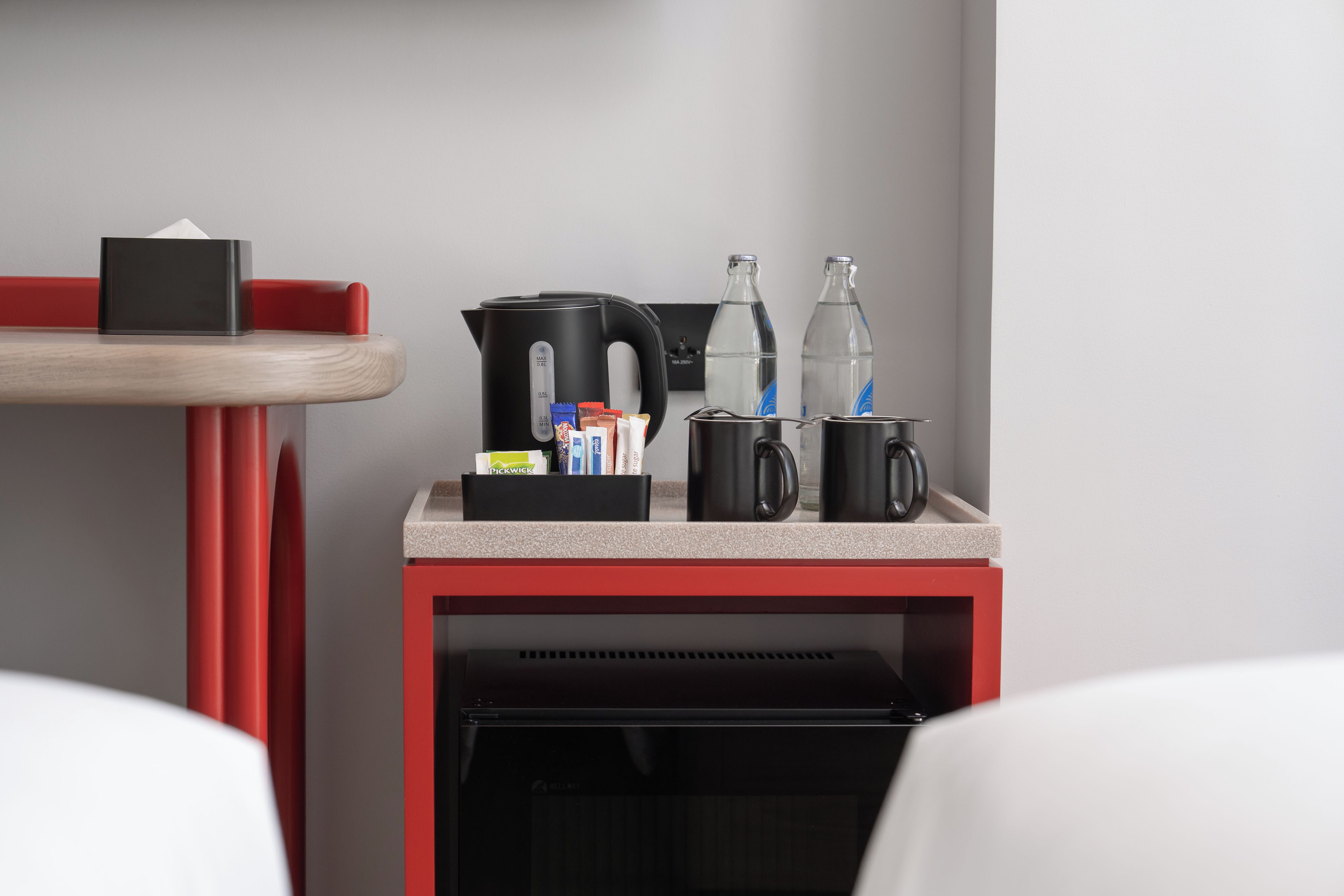 Eine Küchenzeile mit einer Kaffeemaschine, einem Wasserkocher, einer Wasserflasche und einer Tasse auf einer Arbeitsfläche.