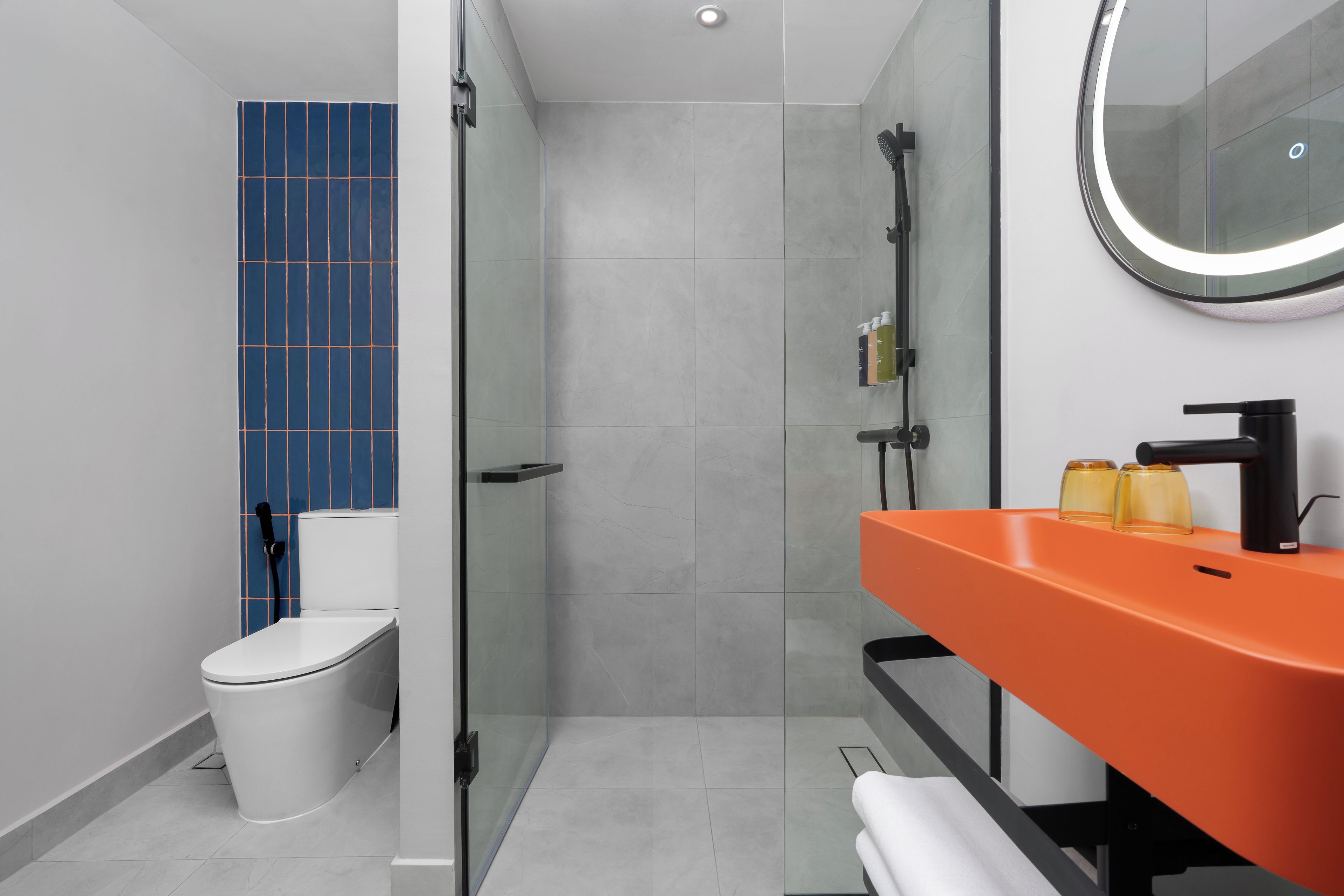 A modern bathroom with a glass-enclosed shower, a white toilet, and an orange sink with a mirror above it.