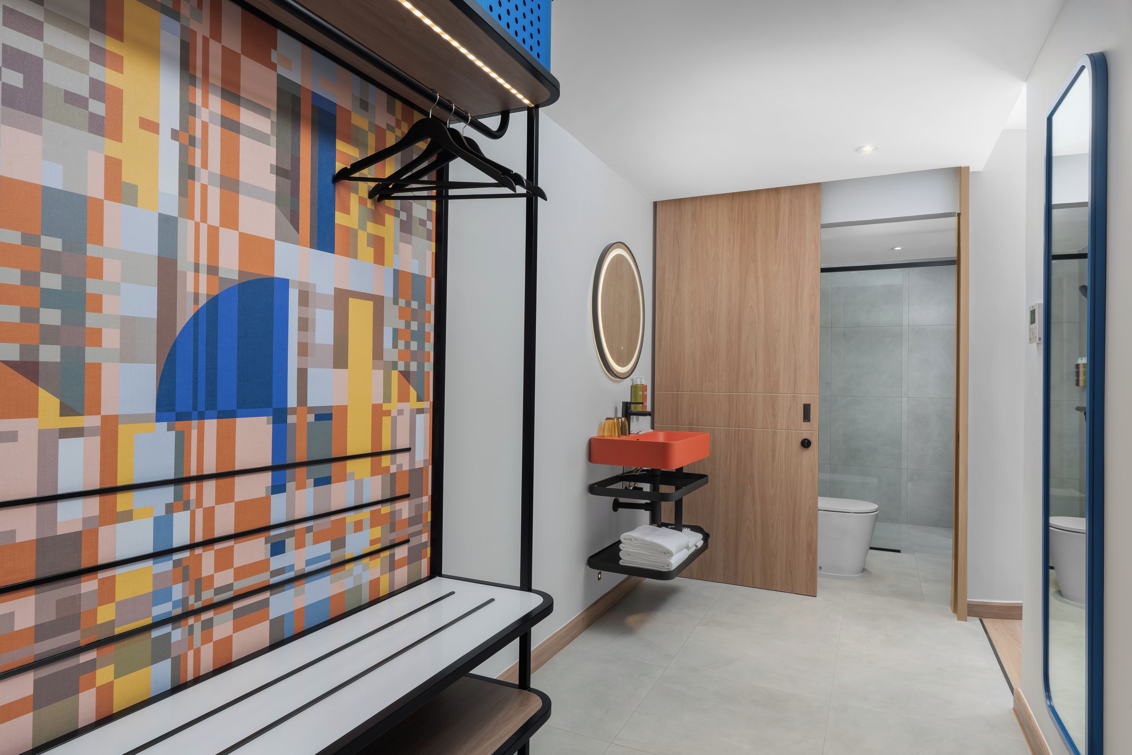 Ein modernes Badezimmer mit gefliestem Boden, einer Holztür, einem Spiegel und einem Waschbecken mit roter Schale.