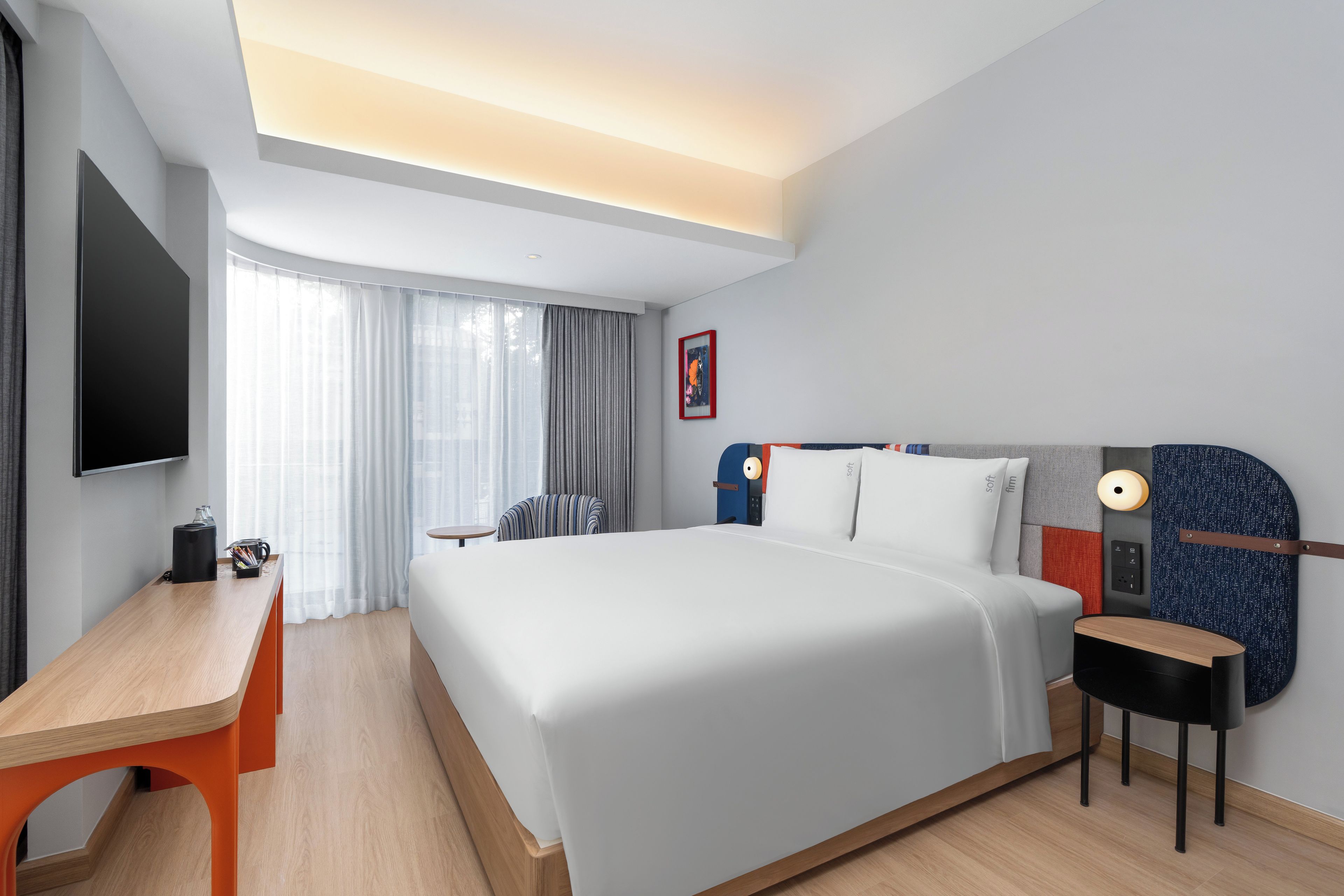 Une chambre d’hôtel moderne avec un grand lit, un bureau, une chaise, une télévision et une fenêtre avec des rideaux.