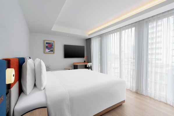 A modern hotel room with a large bed, a flat-screen TV mounted on the wall, a small table, and a large window with sheer curtains. - Holiday Inn Express Bangkok Sukhumvit Thonglor by IHG (Bangkok)
