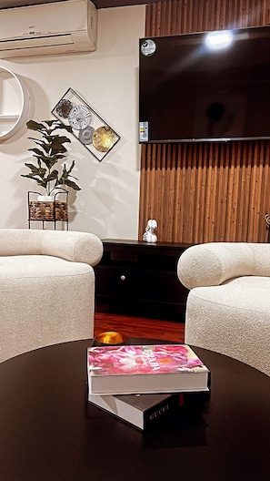 Una sala de estar moderna con un sofá, una mesa de centro con un libro, un televisor de pantalla plana, decoración de pared y un panel de pared de madera.
