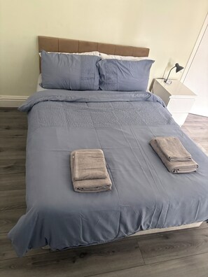 Un letto rifatto con una coperta blu, due cuscini e asciugamani piegati.