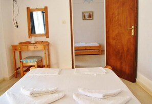 Ein Schlafzimmer mit einem Bett, einer Holzkommode, einem Stuhl, einem Spiegel und einer Tür.