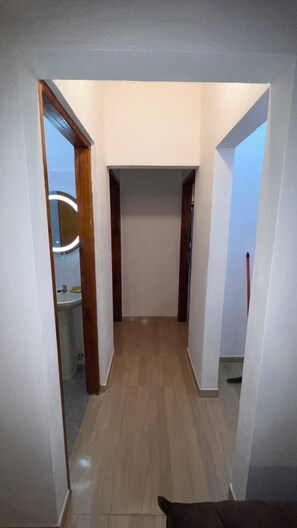 A hallway with a wooden floor, white walls, and a door leading to a bathroom with a mirror and sink.