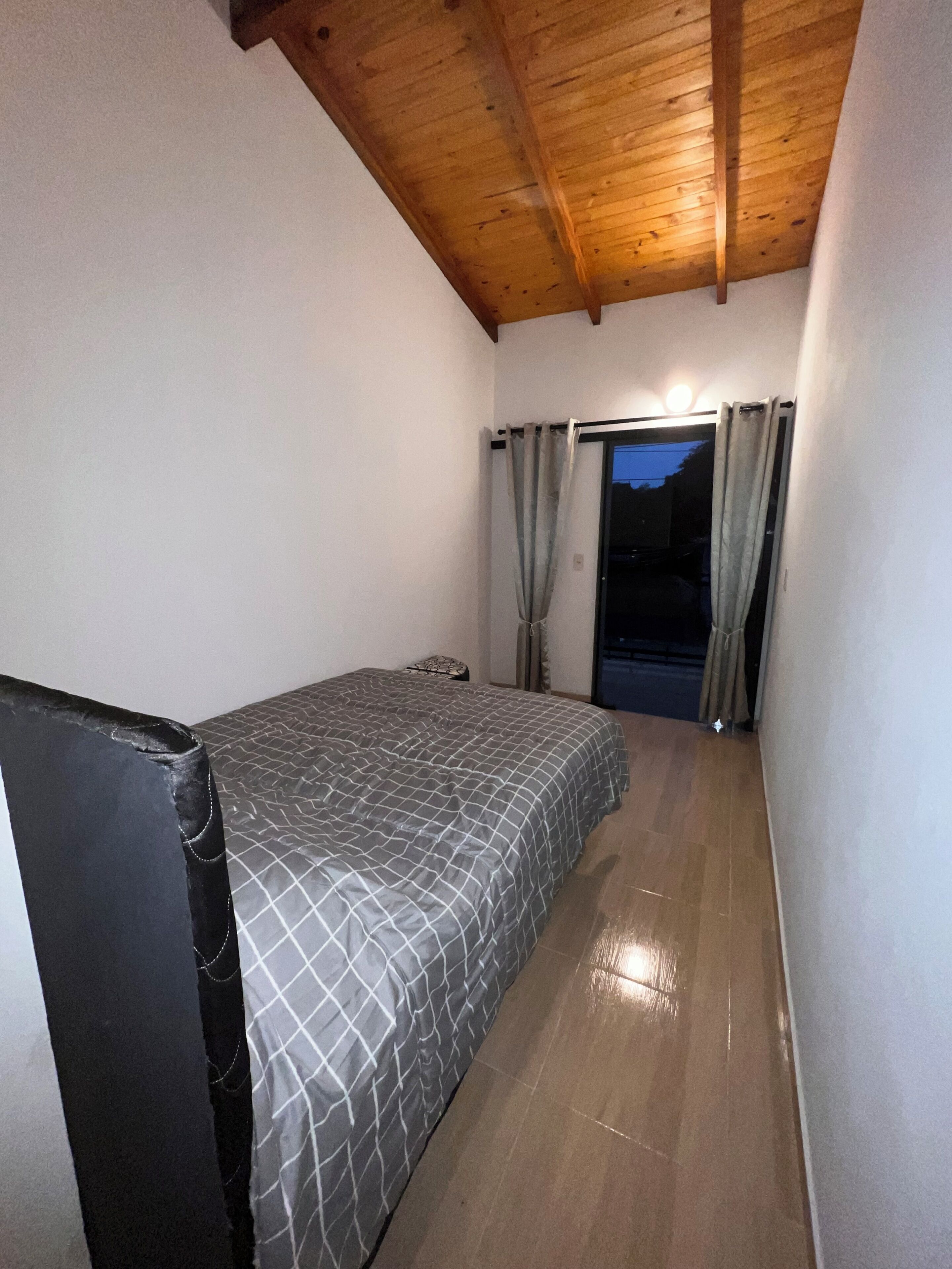 Un dormitorio con cama, ventana con cortinas y techo de madera.