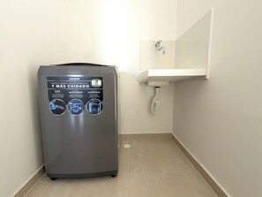 A compact, gray, wall-mounted washing machine with a control panel featuring a touch screen and three circular indicators.