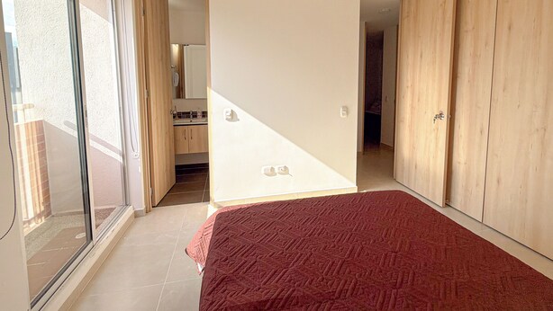 Un dormitorio con una cama grande, puertas de cristal correderas que dan a un balcón y un armario de madera.
