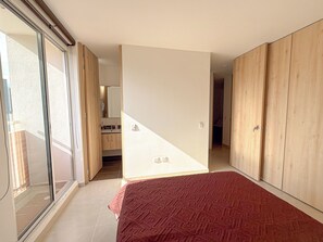 Een slaapkamer met een groot bed, glazen schuifdeuren naar een balkon en een houten garderobe.