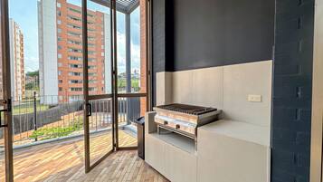 A balcony with a grill, a view of buildings, and a tiled floor.
