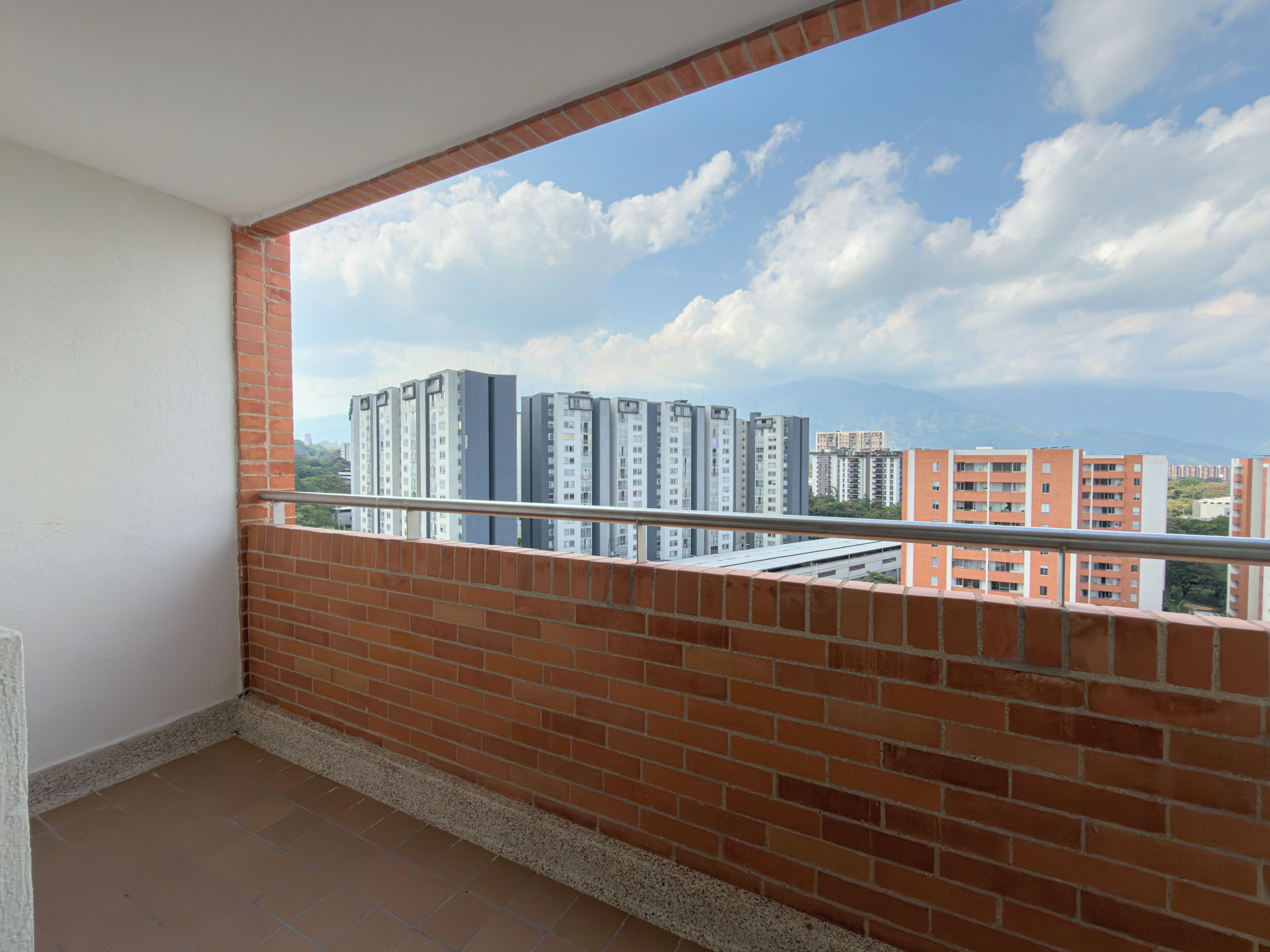 A balcony with a clear view of high-rise buildings and a blue sky with clouds.