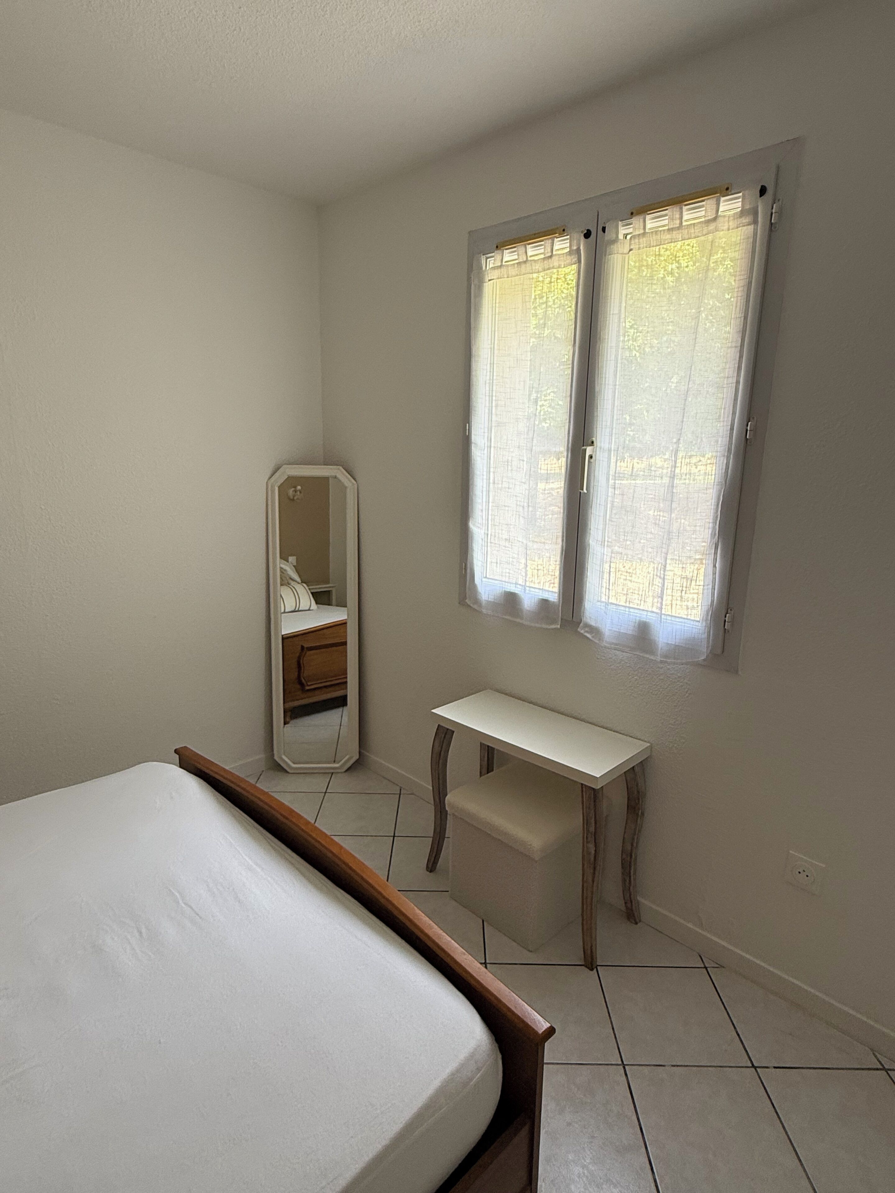 Ein Schlafzimmer mit einem Bett, einem Schreibtisch, einem Spiegel und einem Fenster mit Vorhängen.