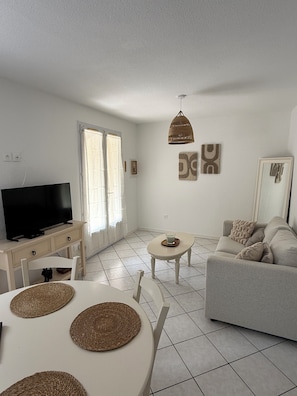 A living room with a television, a sofa, a dining table with placemats, and a ceiling light fixture.