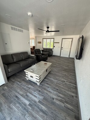 A spacious living room with a gray leather sofa, a wooden coffee table, and a ceiling fan. - Cozy 2-bedroom house in serene Glendo (Glendo)