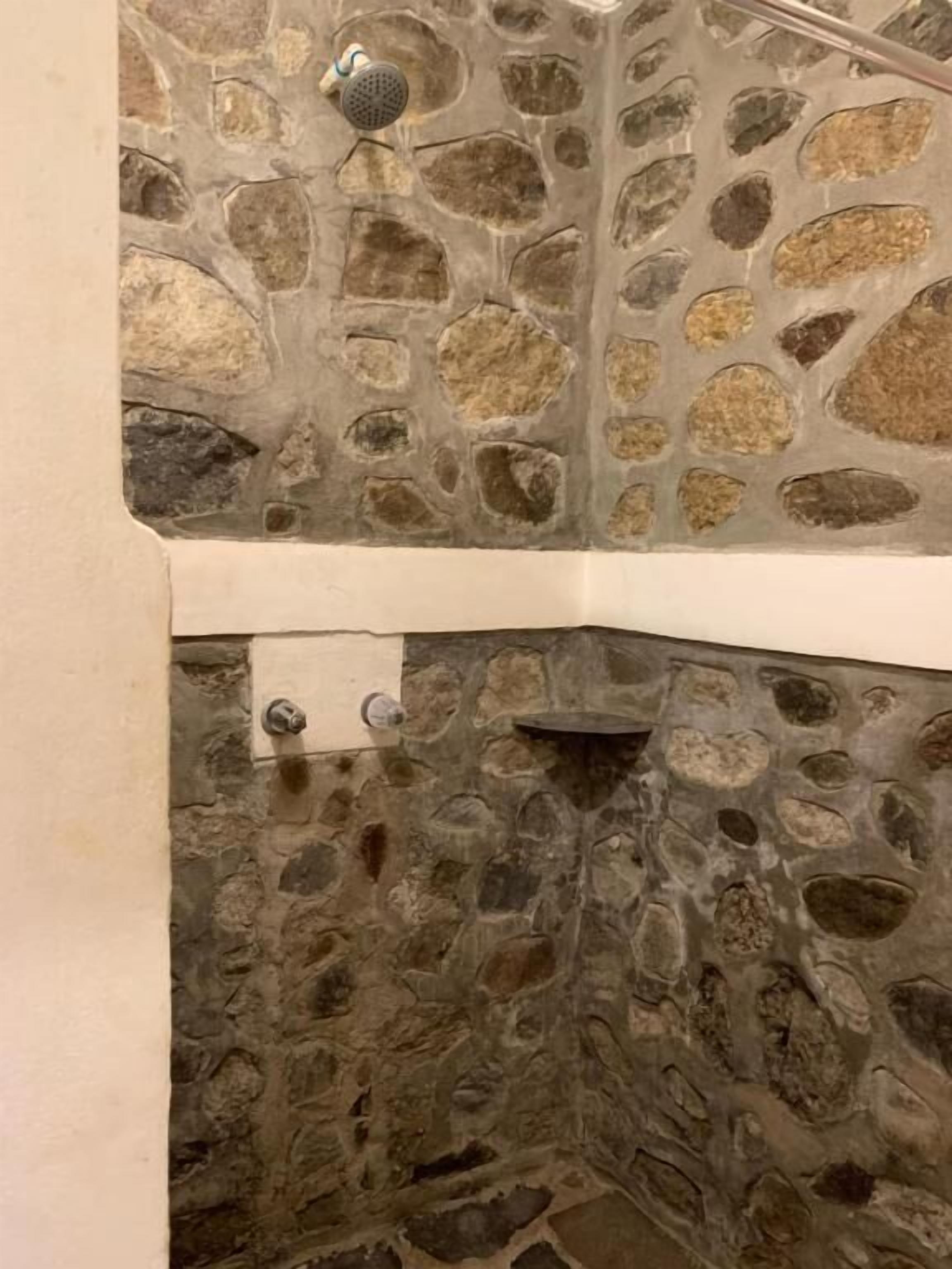 A stone shower enclosure with a handheld showerhead.