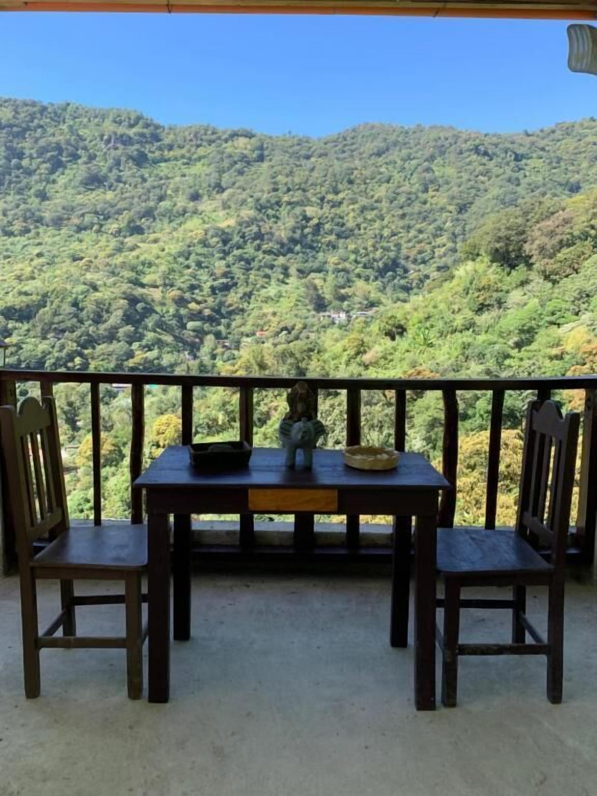 A balcony with a table and chairs overlooking a mountainous landscape.