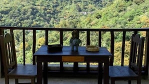 A balcony with a table and chairs overlooking a mountainous landscape. - Hostal Xeabaj La Cascada (Santa Cruz La Laguna)