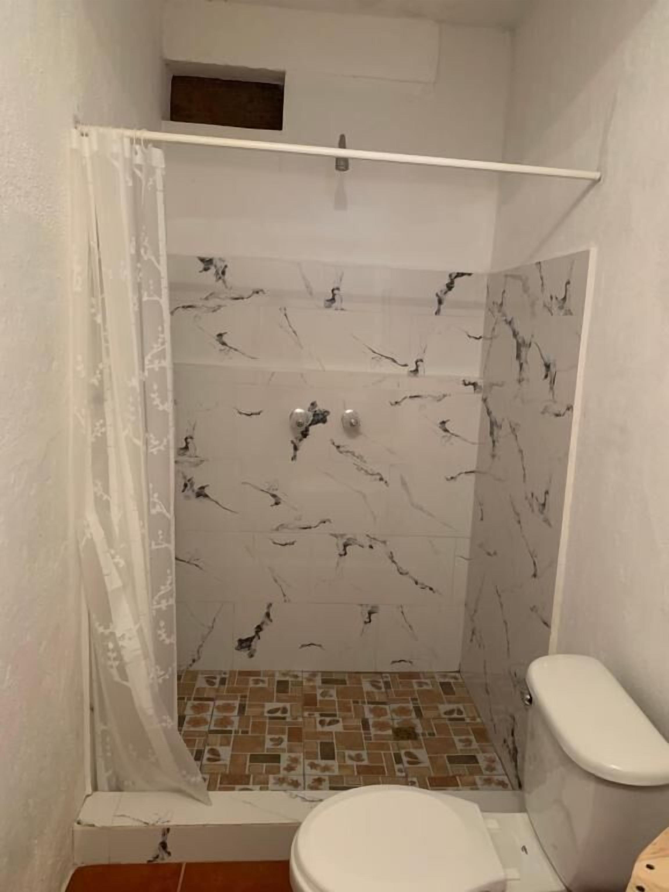 Un baño pequeño con ducha, inodoro y piso de azulejos.