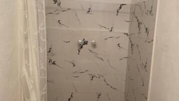 Un baño pequeño con ducha, inodoro y piso de azulejos.