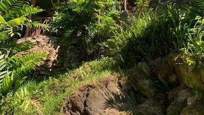 A building with a sloped roof, surrounded by lush greenery and a rocky landscape. - Hostal Xeabaj La Cascada (Santa Cruz La Laguna)