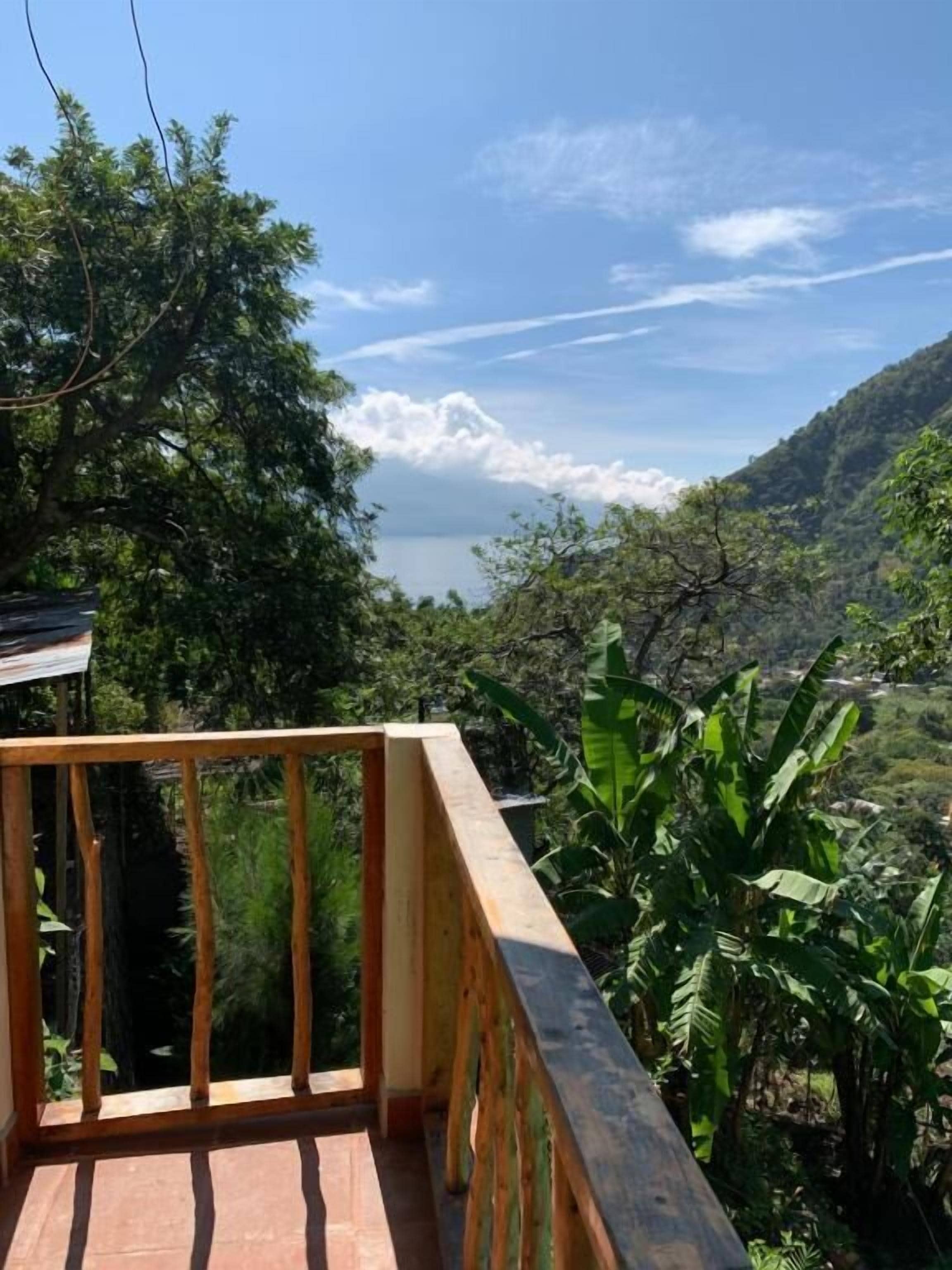 Varanda de madeira com vista para uma paisagem montanhosa e um corpo de água.