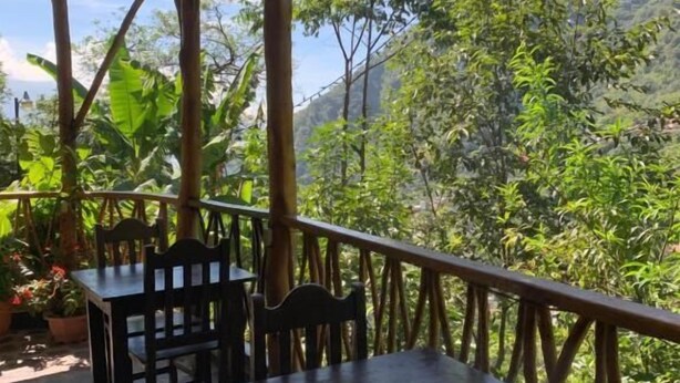 An outdoor patio with stone flooring, wooden tables and chairs, and a view of a mountainous landscape. - Hostal Xeabaj La Cascada (Santa Cruz La Laguna)