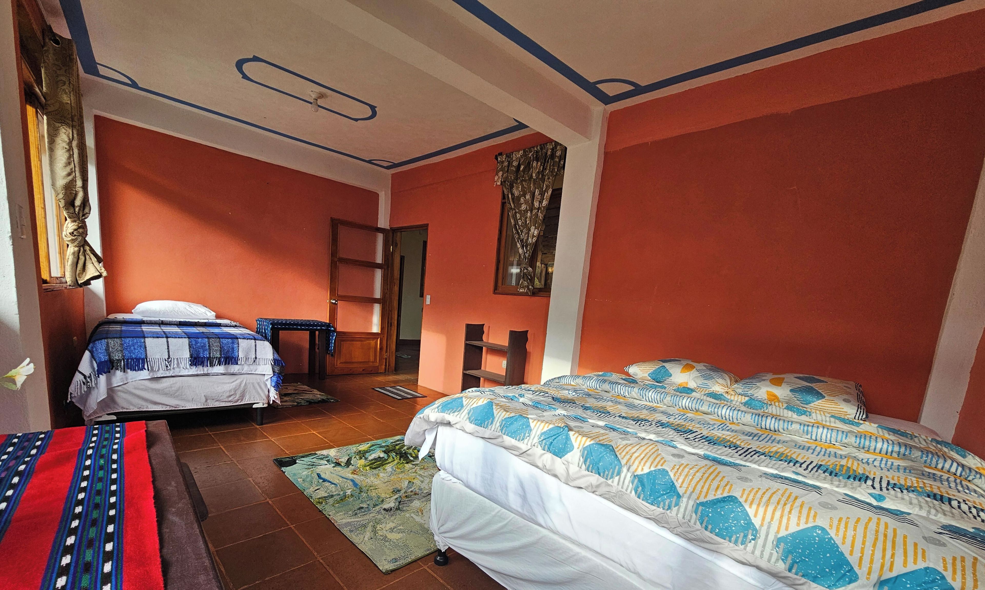 A room with two beds, a wooden door, a small table, and a patterned rug.