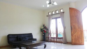 Un salon avec un canapé, une table basse, un lustre, une porte en bois et une vue par la fenêtre.