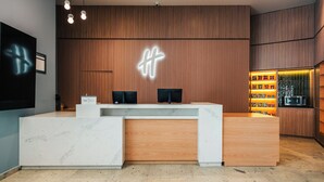 A reception desk with a wooden finish and a marble base, a neon sign above, and a snack display to the right. - Holiday Inn Mexicali Centro Civico by IHG (Mexicali)