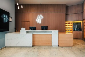 A reception desk with a wooden finish and a marble base, a neon sign above, and a snack display to the right. - Holiday Inn Mexicali Centro Civico by IHG (Mexicali)