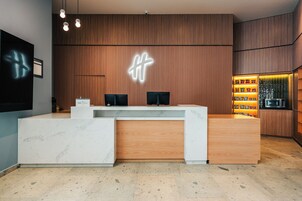 Un mostrador de recepción con detalles de madera y una base de mármol, un letrero de neón arriba y una exhibición de snacks a la derecha.