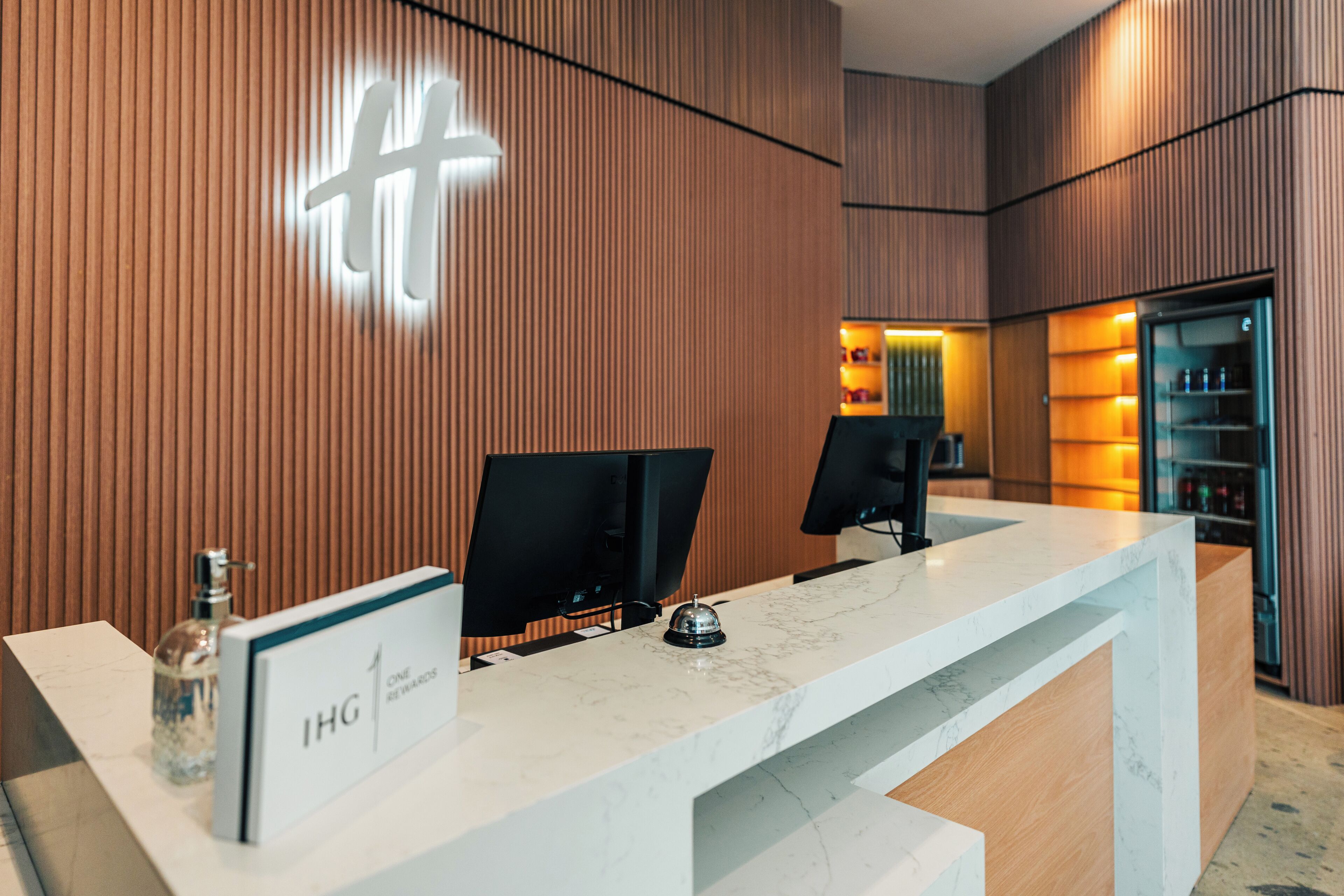 Un mostrador de recepción de diseño moderno, con encimera de mármol y un panel de pared de madera que muestra un logotipo.