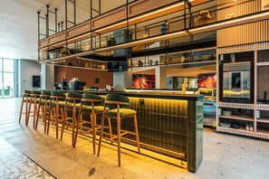 Zona de bar moderna con taburetes altos, barra y cocina al fondo.