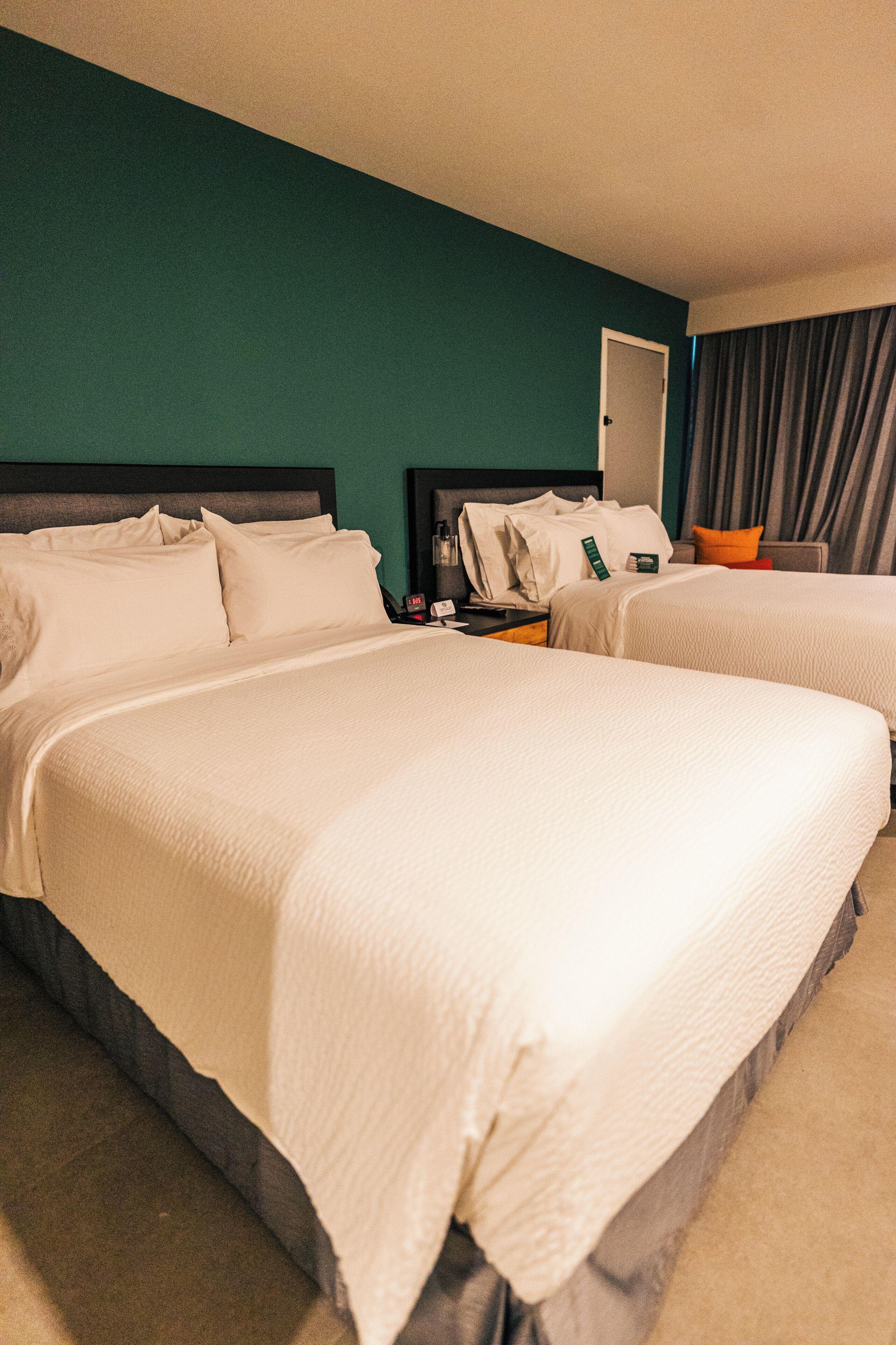 A hotel room with two beds, a nightstand, a mirror, and a window with curtains.
