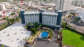 A high-rise hotel with multiple floors, a rooftop pool, and a well-maintained surrounding landscape.