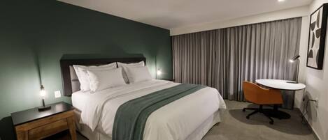 Una habitación de hotel con cama, mesita de noche, lámpara, silla y una pequeña mesa con lámpara.