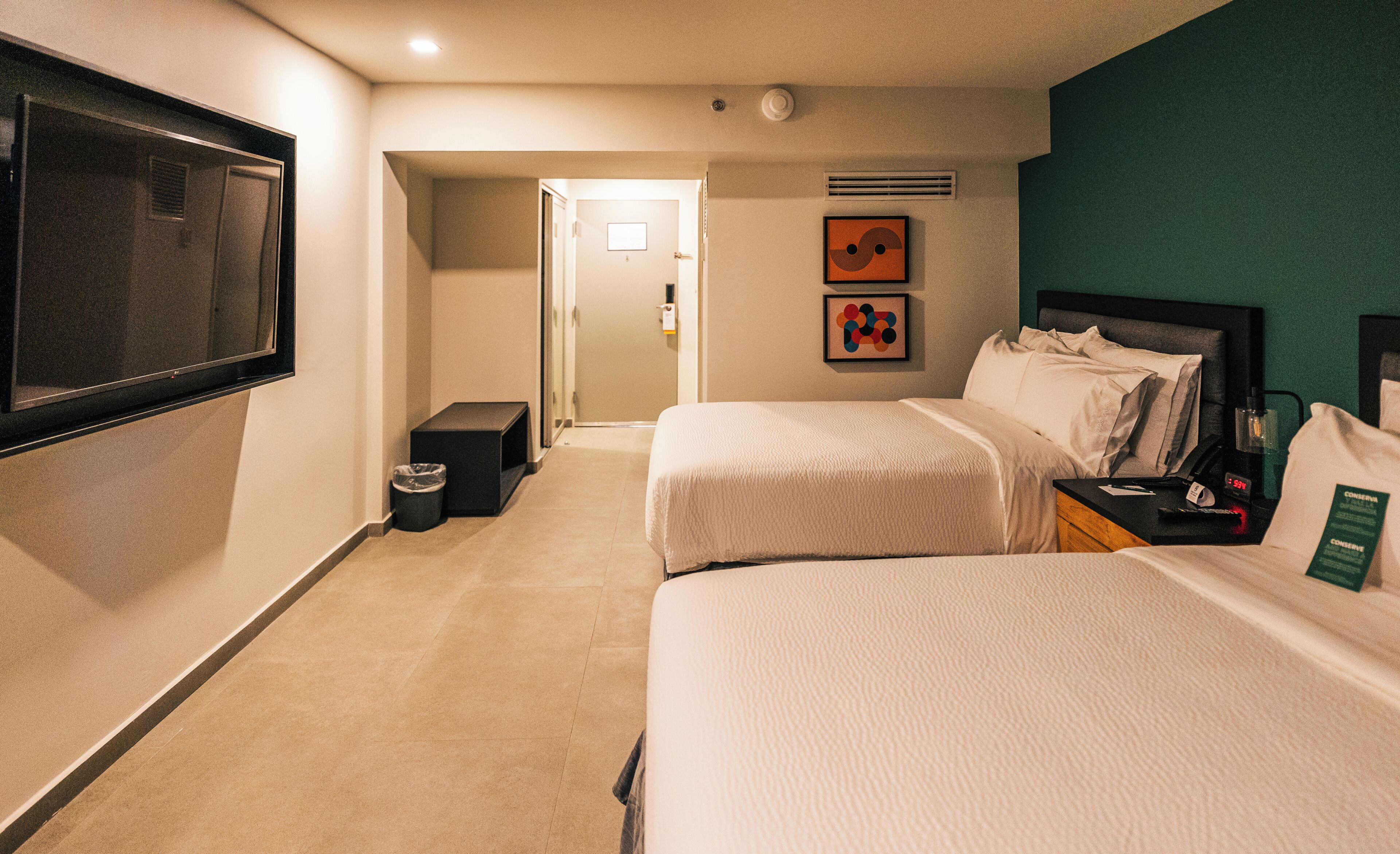 A hotel room with two beds, a TV, a small table, and artwork on the wall.