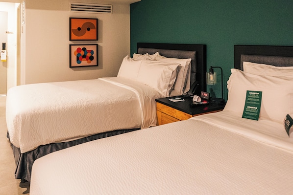 A hotel room with two beds, a nightstand, a clock, and artwork on the wall.